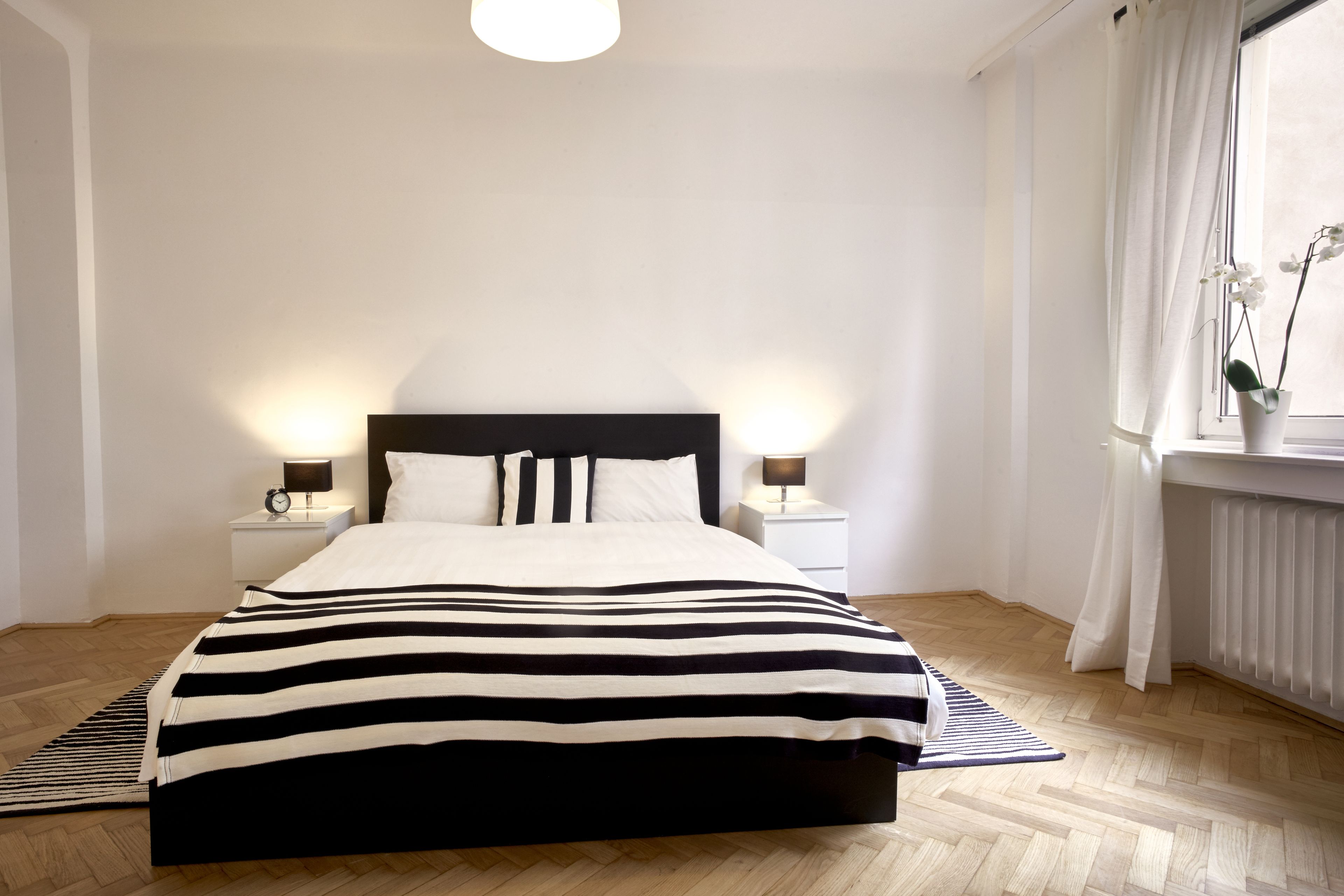 Un lit bien fait, recouvert d’une couvre-lit à rayures, avec deux lampes de chevet et une fenêtre avec des rideaux.