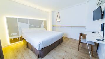 Una habitación de hotel moderna con una cama grande, un escritorio con silla, un televisor y un espejo en la pared.