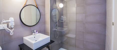 A modern bathroom with a glass-enclosed shower, a round mirror, and a white sink on a black countertop.