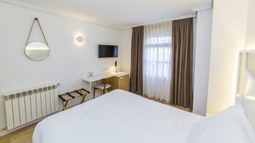 A hotel room with a large bed, a desk with a chair, a television, and a window with curtains.