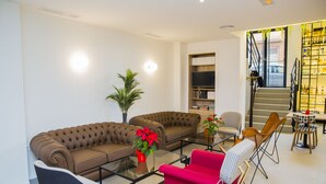 Een moderne woonkamer met twee bruine banken, een rode fauteuil, een glazen salontafel en een boekenkast.