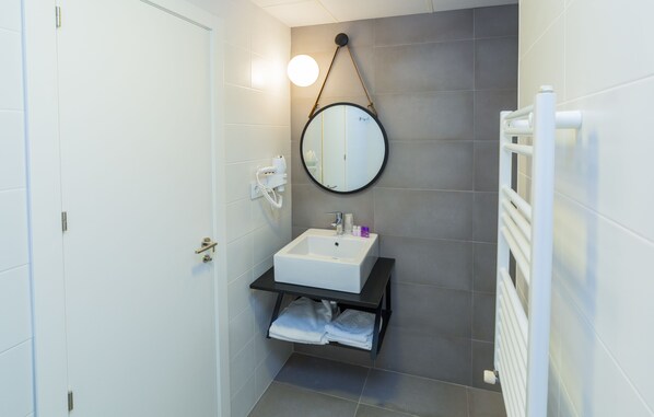 A bathroom with a white sink, a round mirror, a towel rack, and a towel dispenser.