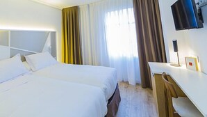 Een hotelkamer met een groot bed, nachtkastje, televisie en een raam met gordijnen.