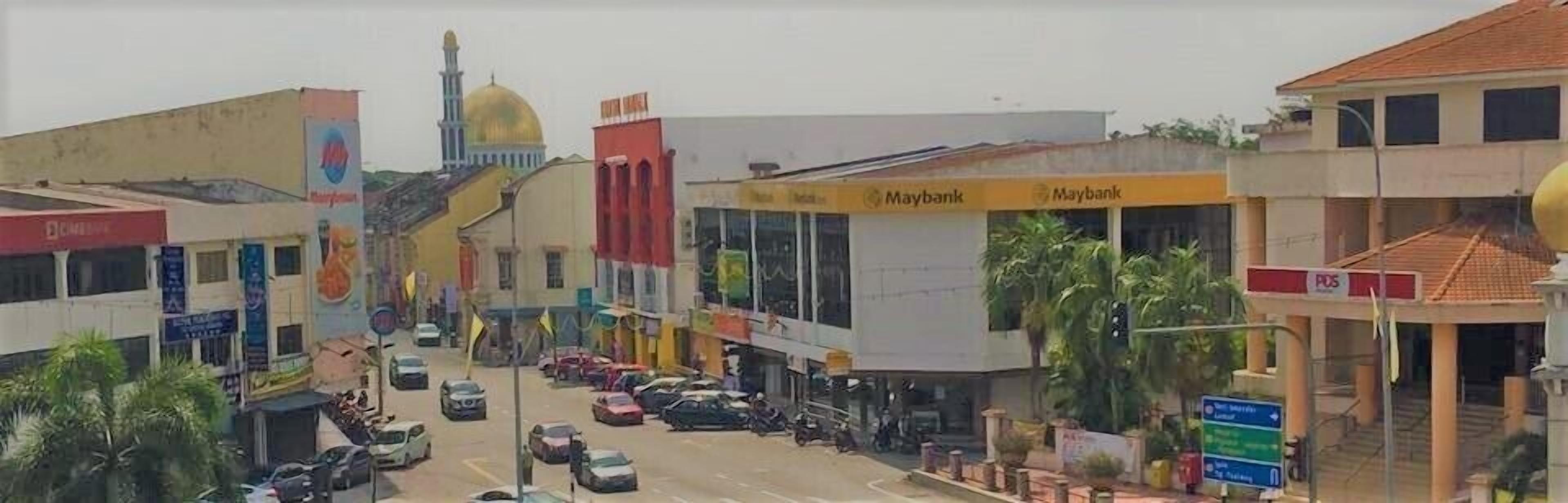 A street view with various buildings, including a bank with a Maybank sign, and a mosque with a golden dome.