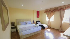 A bedroom with a bed, a chair, a nightstand, and a window with curtains. - Royale Hotel (Batu Gajah)