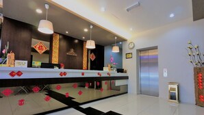 A hotel reception area with a check-in counter, decorative wall hangings, a clock, and an elevator. - Royale Hotel (Batu Gajah)