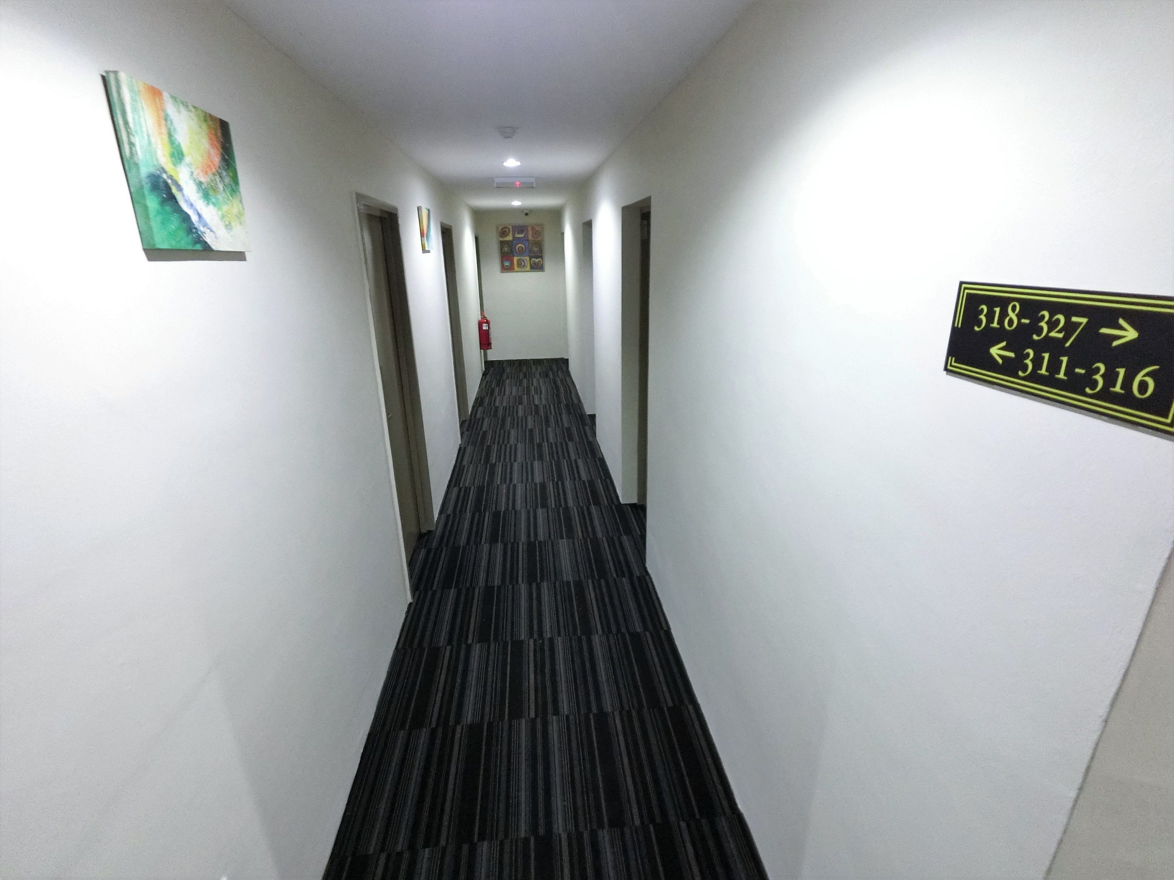 A hotel hallway with directional signs, a fire extinguisher, and a colorful abstract painting on the wall.