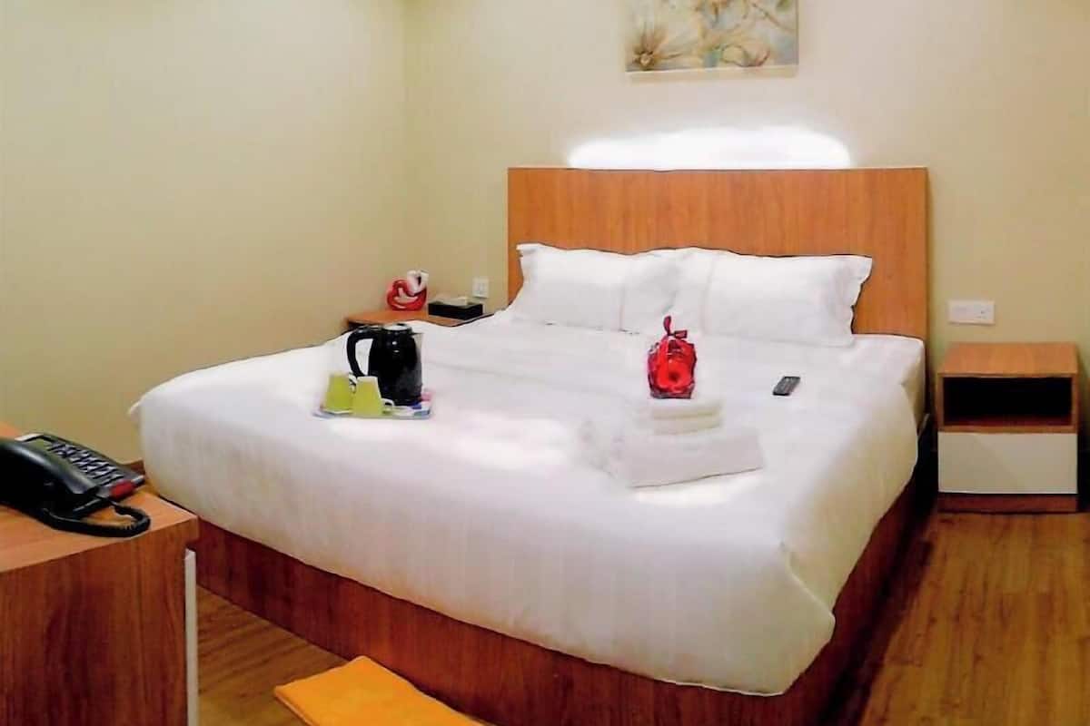 A hotel room with a bed, bedside table, and a small wooden nightstand.