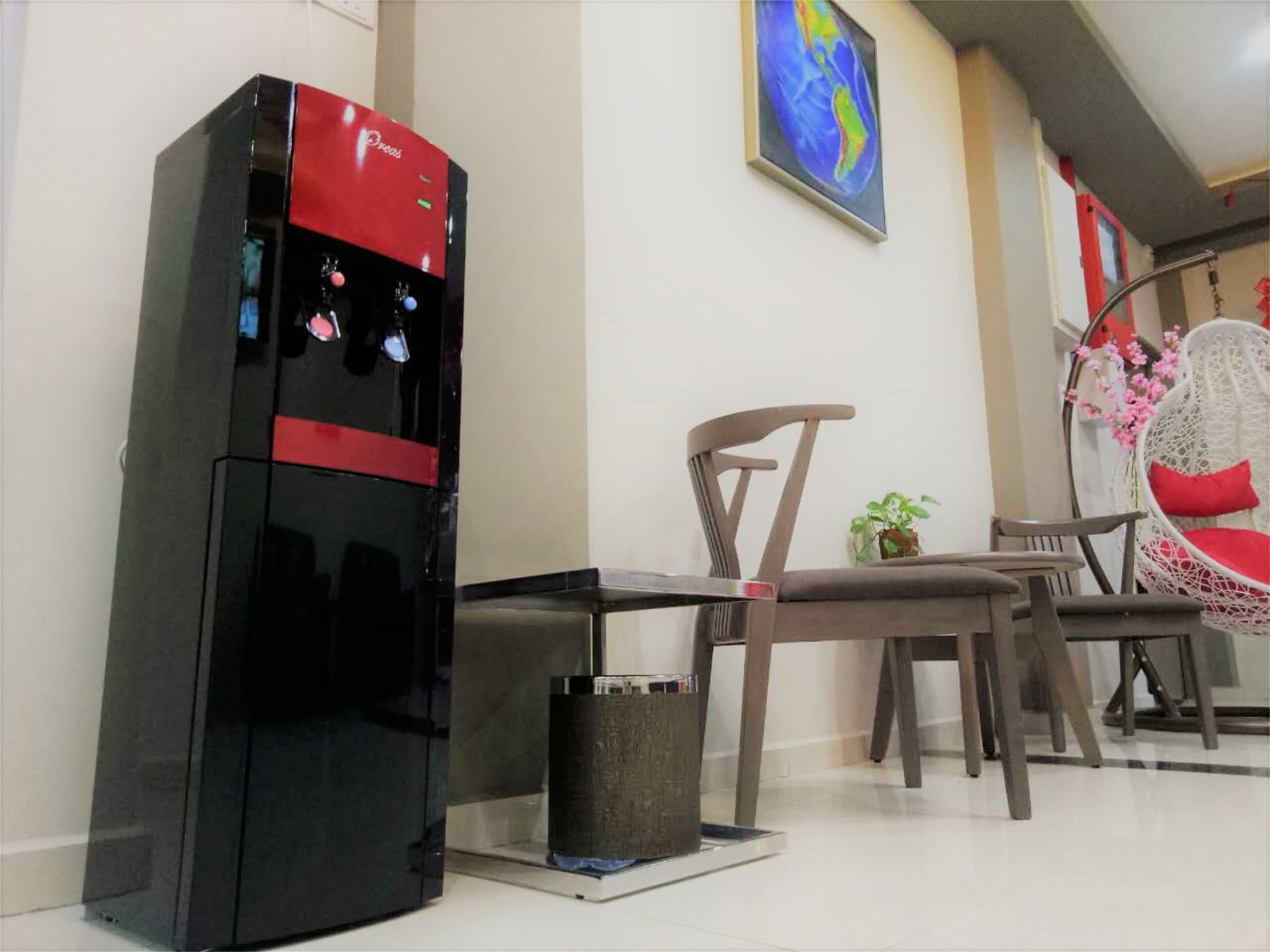 Una kitchenette compacta con un refrigerador negro y rojo, un pequeño bote de basura y una zona de comedor con una silla y una mesa.