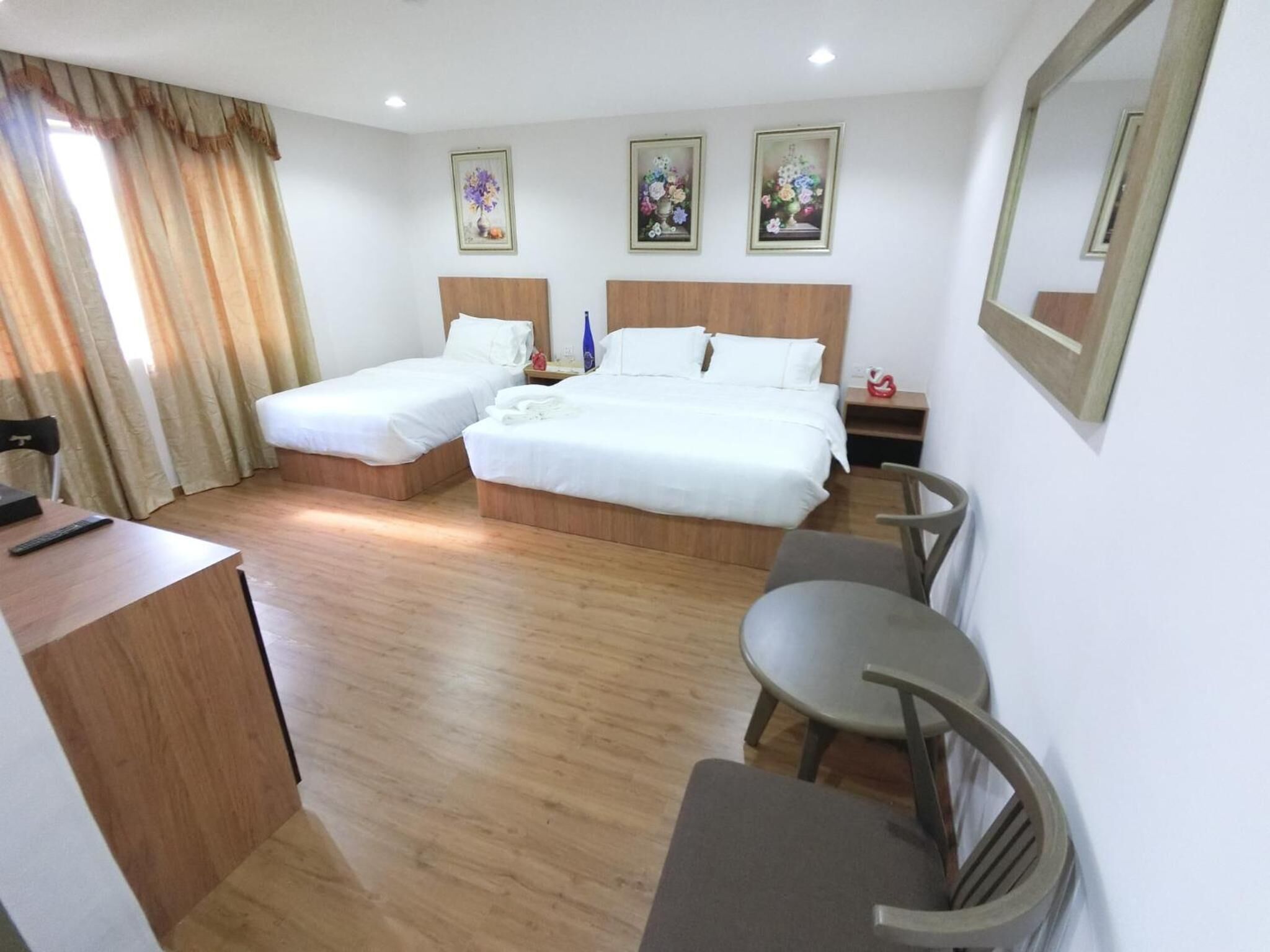 A hotel room with two single beds, a desk, a chair, and a small table.