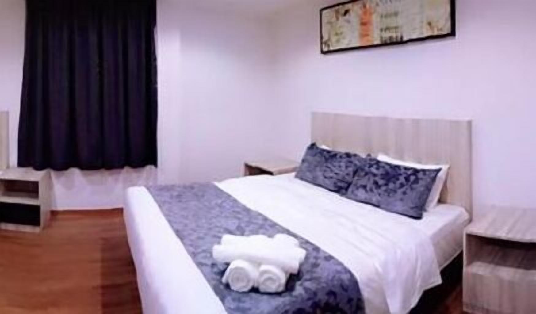 A hotel room with a bed, a nightstand, a small table, and a wall-mounted artwork.