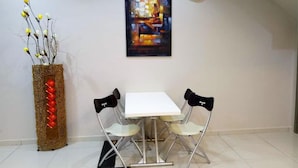 A dining area with a white table and two chairs, a decorative vase with branches, a painting, and a clock on the wall. - Royale Hotel (Batu Gajah)