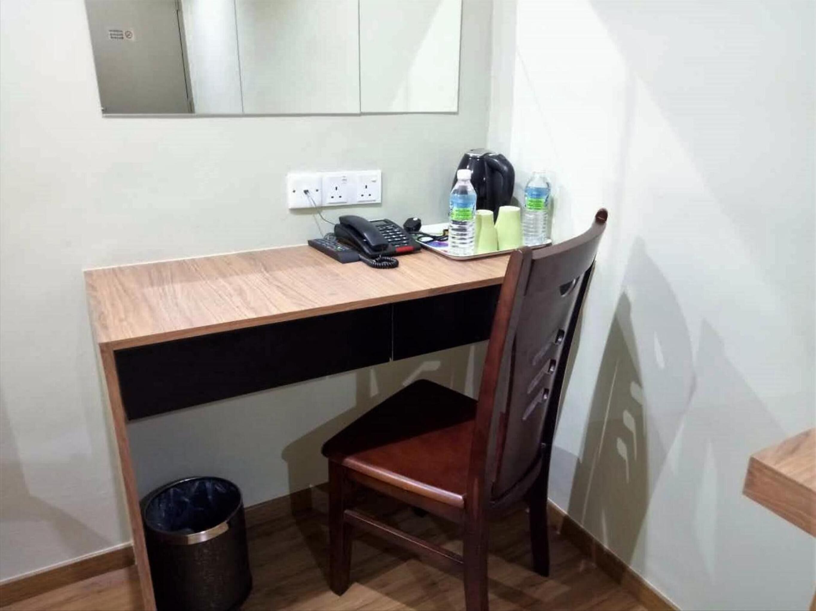 A small office space with a wooden desk, a chair, a telephone, and a trash can.