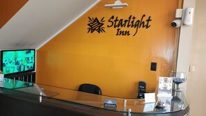 A reception area with a glass counter, a television displaying a room, and a sign reading "Starlight Inn".