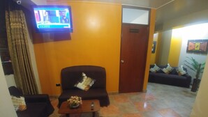 A living room with a sofa, armchair, and a coffee table with a vase. A television is mounted on the wall.