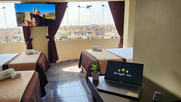 A hotel room with two beds, a laptop, a TV, and a view of the city.