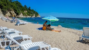 A beach with white lounge chairs and a striped umbrella. - Hotel Vemara Club (Byala)