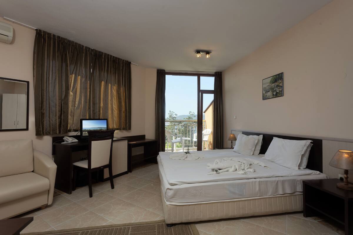 A hotel room with a bed, desk, chair, and a view of the outdoors.