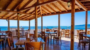 A covered outdoor dining area with wooden tables and chairs, overlooking a body of water. - Hotel Vemara Club (Byala)