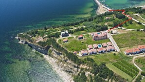 An aerial view of a coastal property with a red path, buildings, and a beach. - Hotel Vemara Club (Byala)