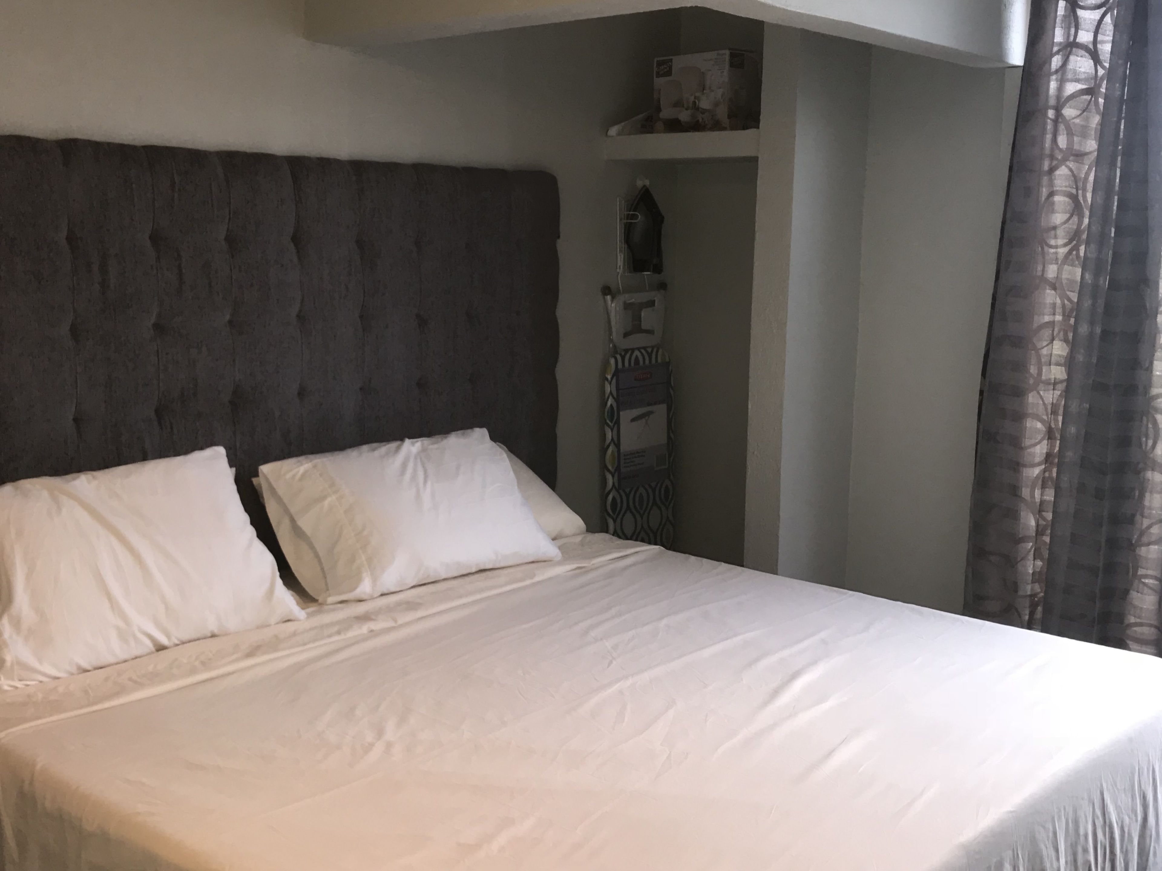 Ein Bett mit weißer Bettwäsche und einem gepolsterten Kopfteil in einem Raum mit neutralen Farben.