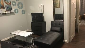 Un espacio habitable compacto con sofá, una mesita, televisor sobre un mueble bajo y un espejo.