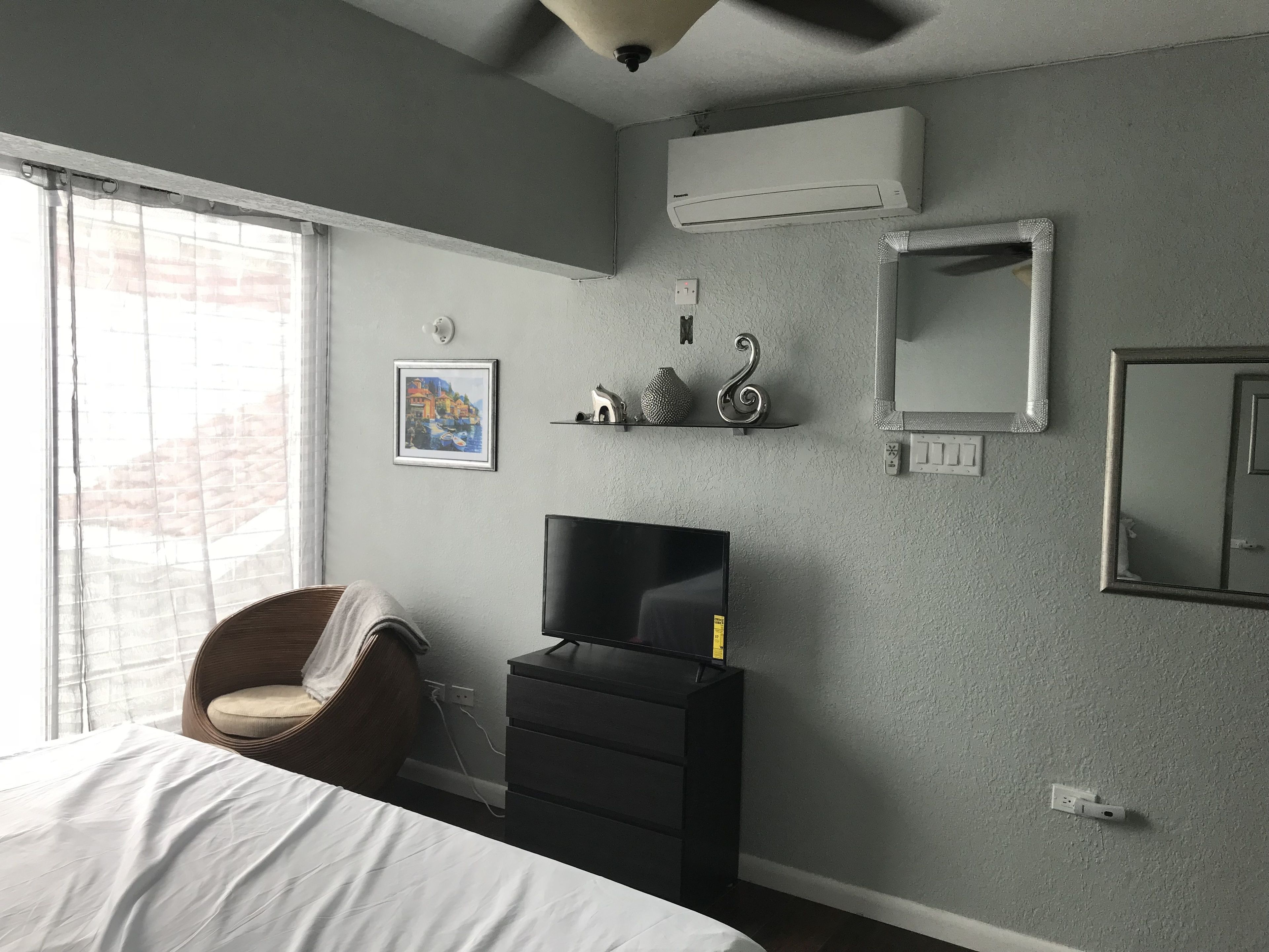 A bedroom with a bed, a TV, a dresser, and a window with curtains.