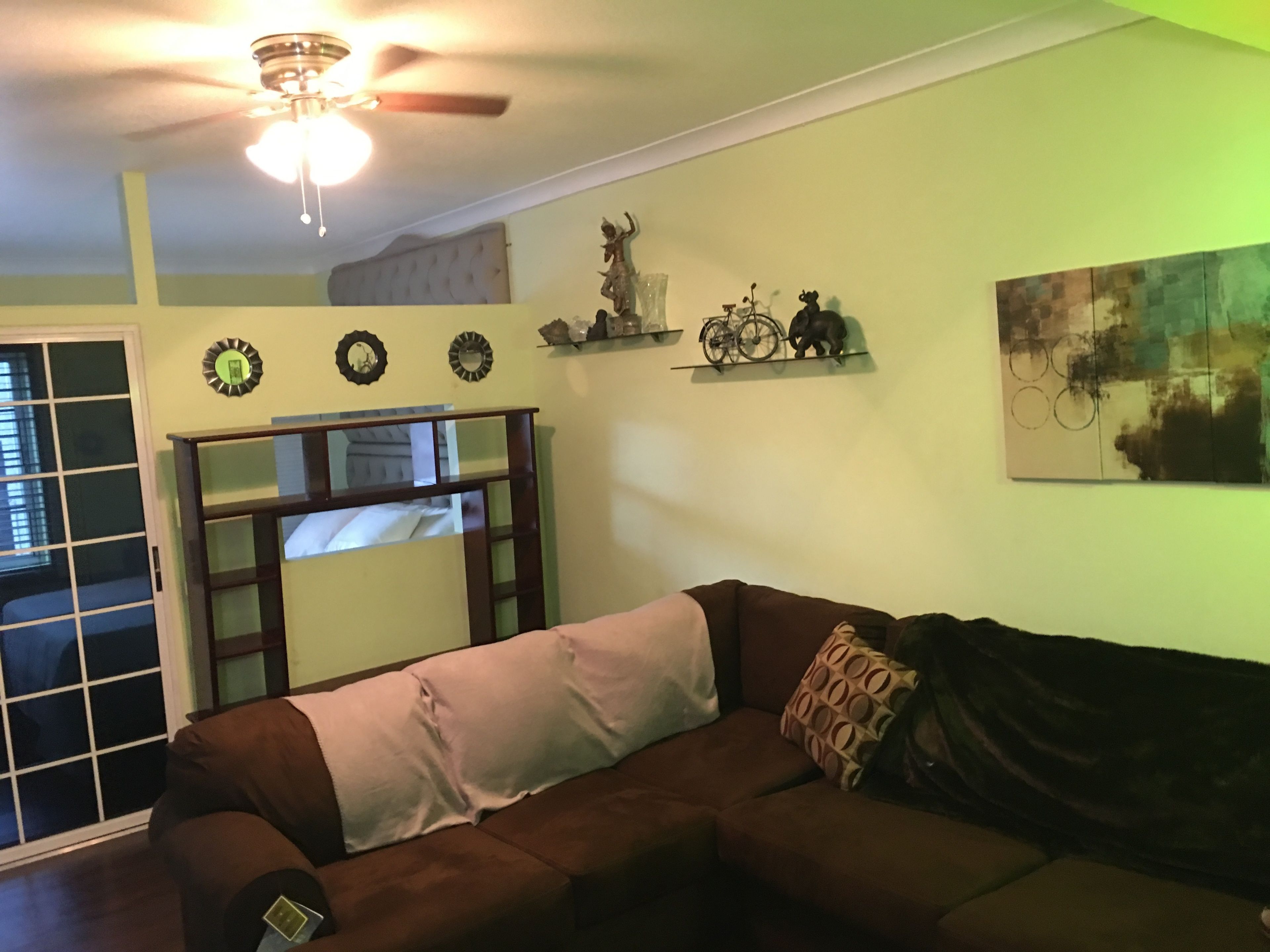 Una sala de estar con un sofá marrón, un ventilador de techo y una ventana con persianas.