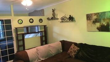Una sala de estar con un sofá marrón, un ventilador de techo y una ventana con persianas.