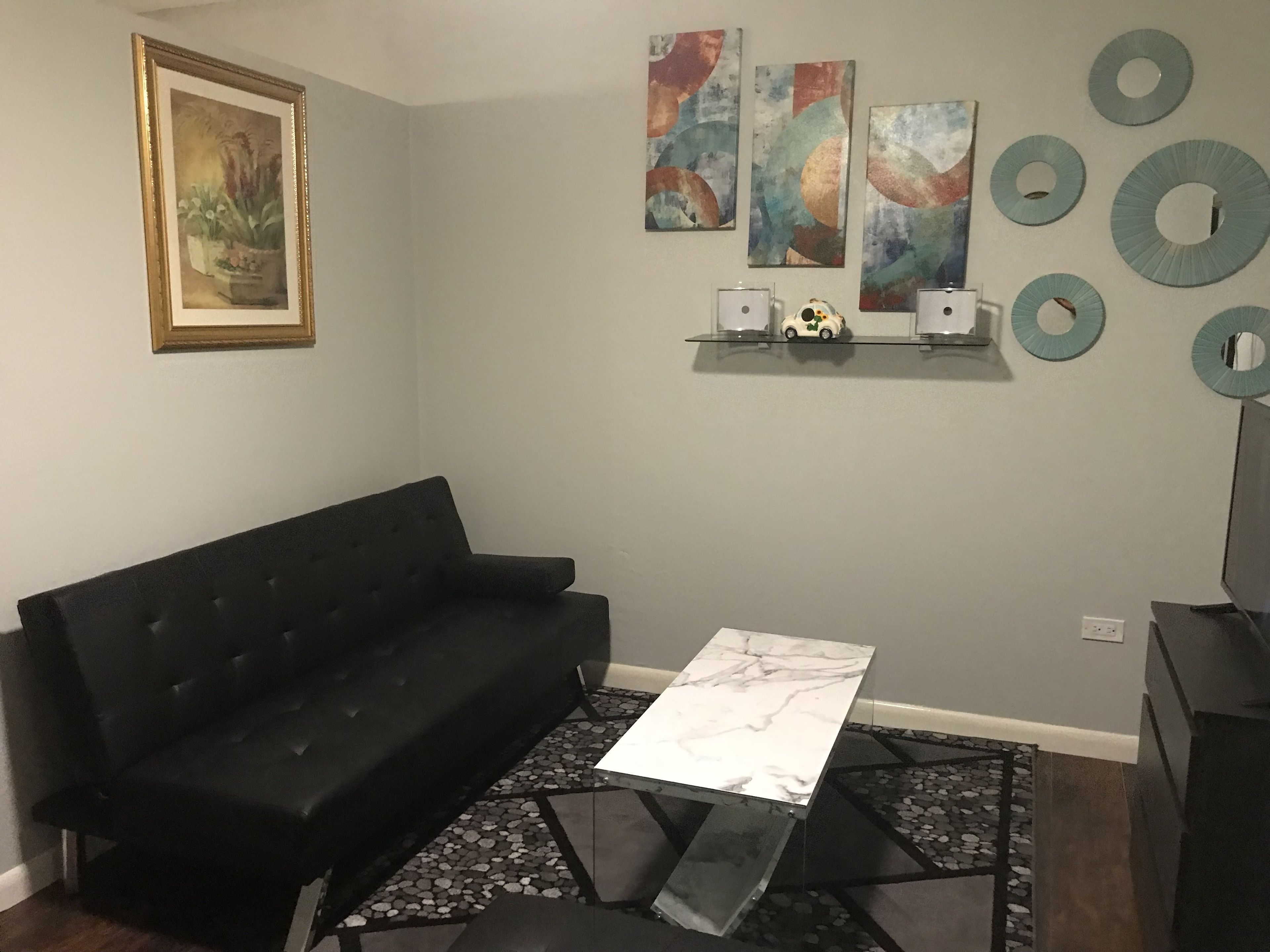 Un salón con un sofá negro, una mesa de centro de mármol, arte abstracto en la pared y espejos decorativos.