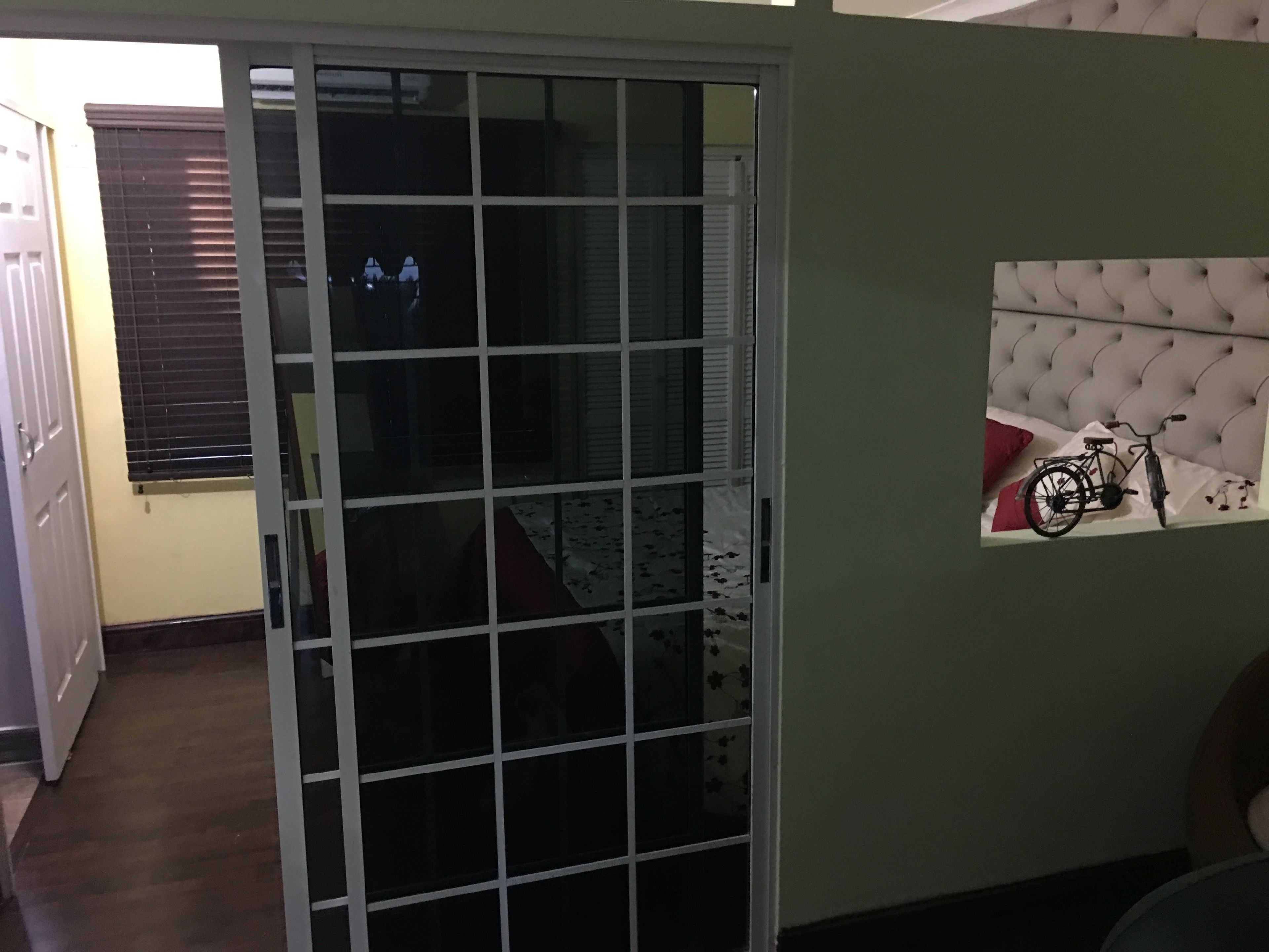 Une chambre dotée d’une porte-fenêtre coulissante donnant sur un balcon, d’une tête de lit capitonnée ornée d’un motif de vélo et d’un tapis à motifs sur le sol.