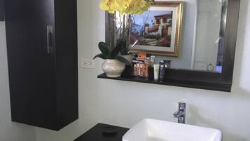 Ein Badezimmer mit einem weißen Waschbecken, dunklen Schränken, einem Spiegel und einer Vase mit gelben Blumen.