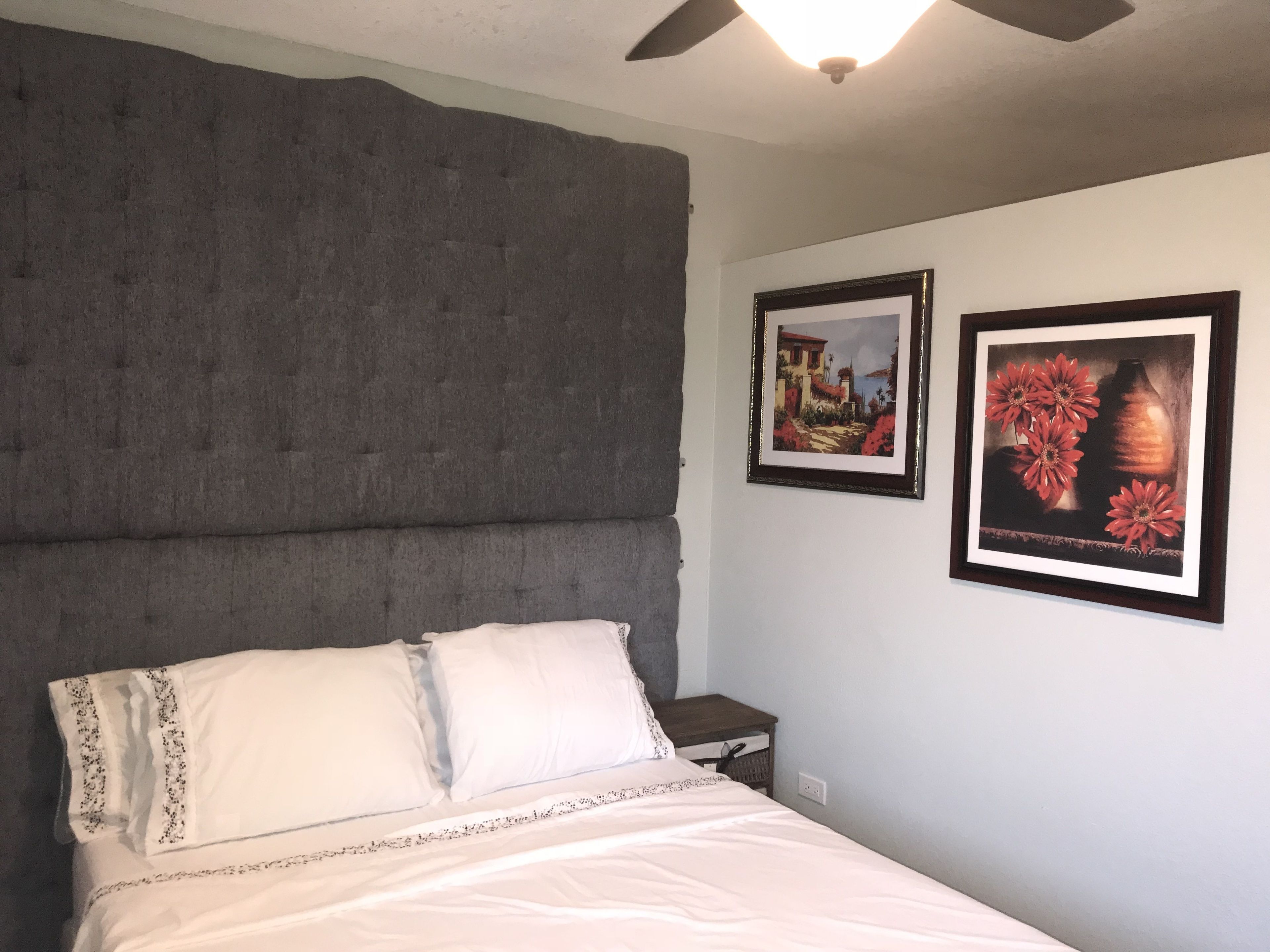 A bedroom with a large bed, a nightstand, and two framed pictures on the wall.