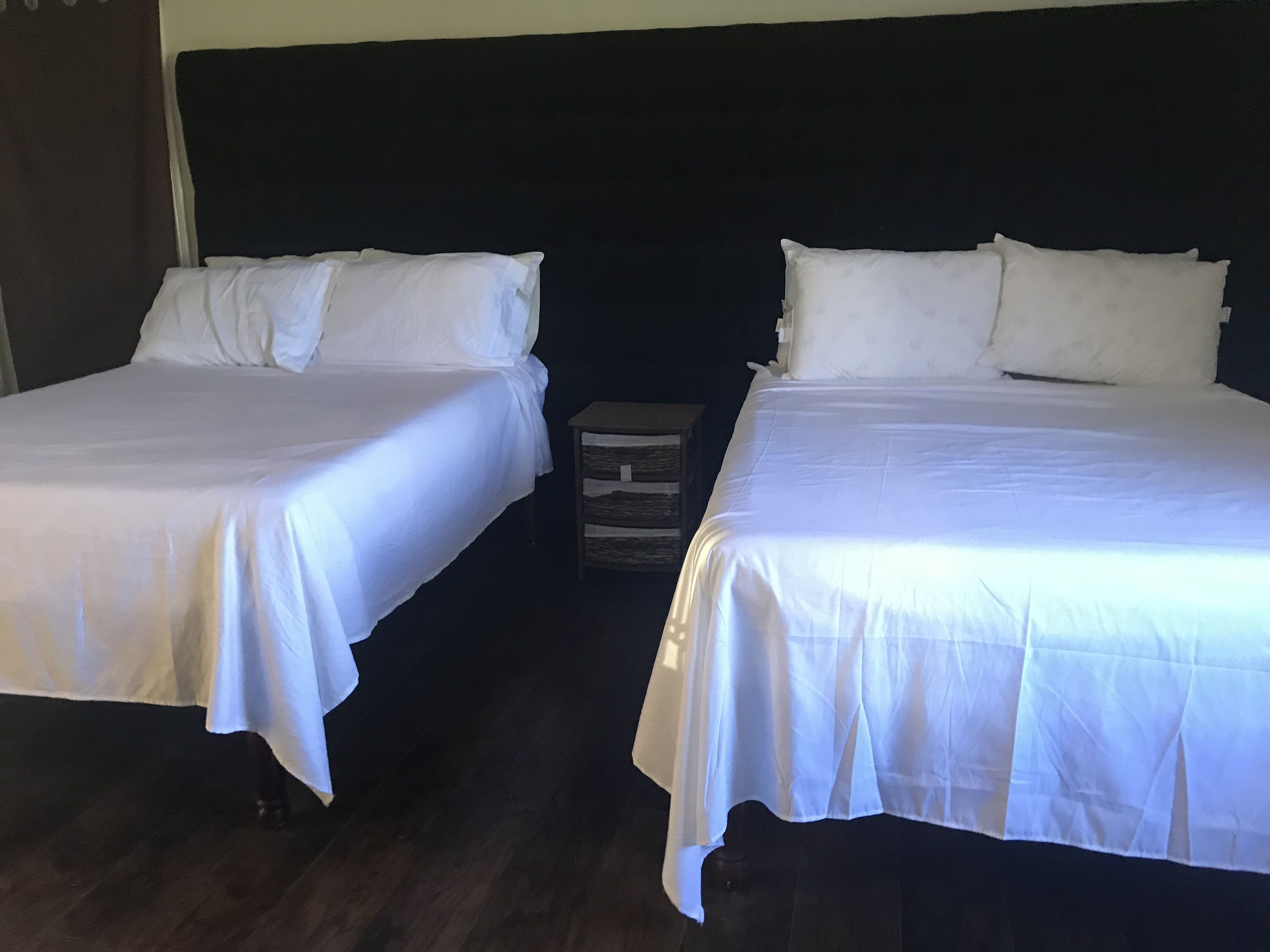 Deux lits simples avec du linge de lit blanc, dans une chambre dotée d’un parquet en bois foncé et d’une tête de lit sombre.