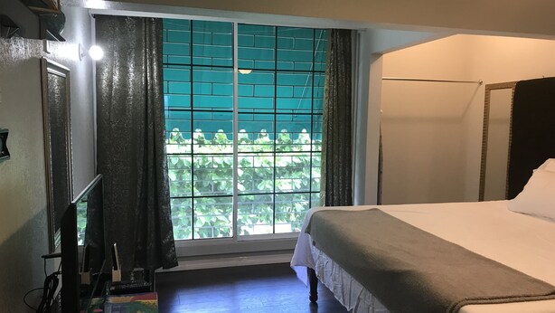 Una habitación de hotel con cama, ventana con cortinas, escritorio con computadora y una silla.