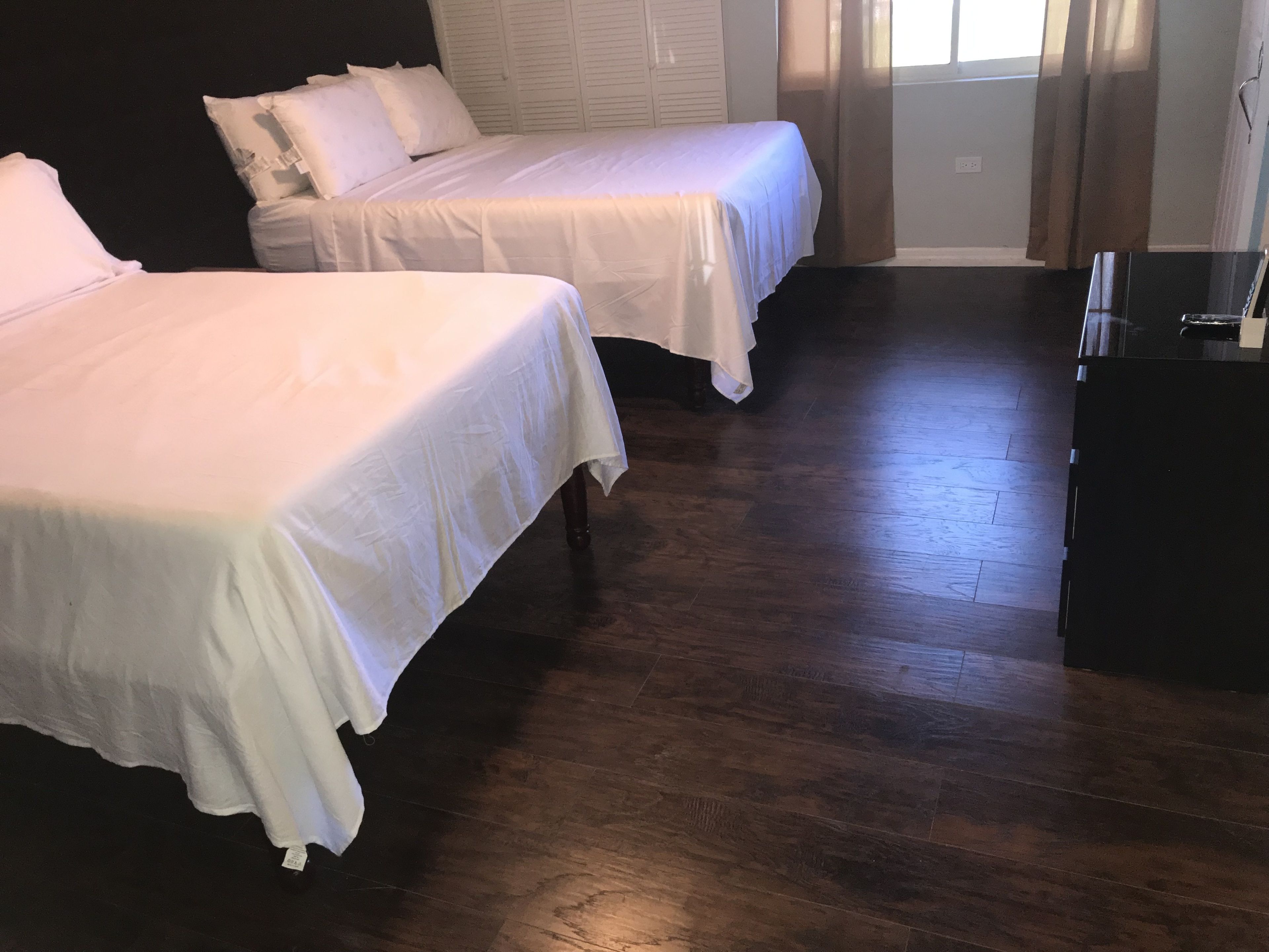 Une chambre avec deux lits, un plancher en bois et une commode de couleur foncée.