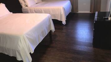 A room with two beds, wooden flooring, and a dark-colored dresser.