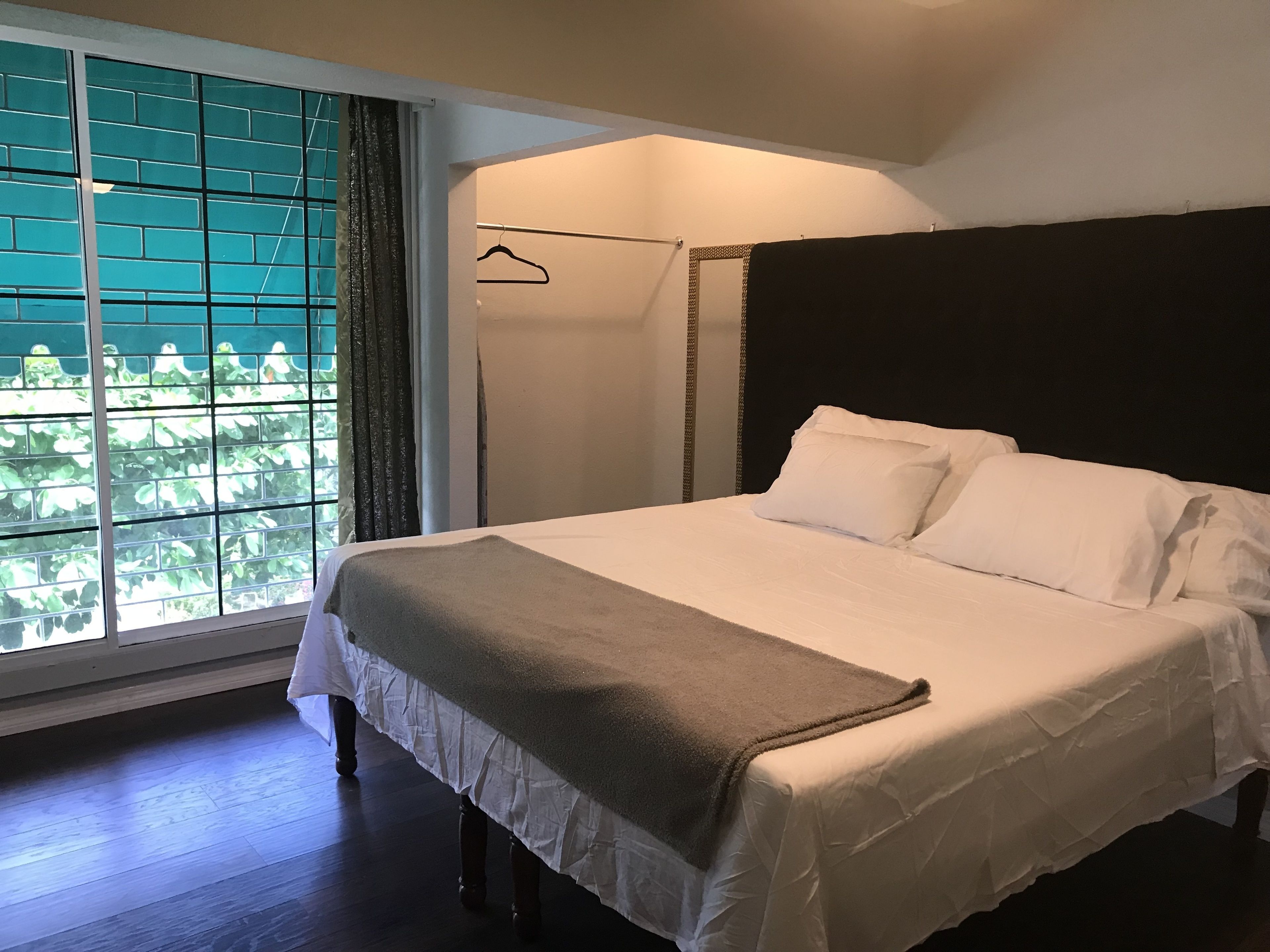 A bedroom with a large bed, a window with curtains, and a view of greenery outside.