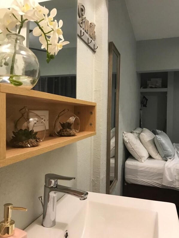 Un baño con lavamanos blanco, un espejo y un estante de madera con adornos.