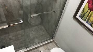 Un baño con cabina de ducha de vidrio, inodoro blanco y un cuadro enmarcado en la pared.