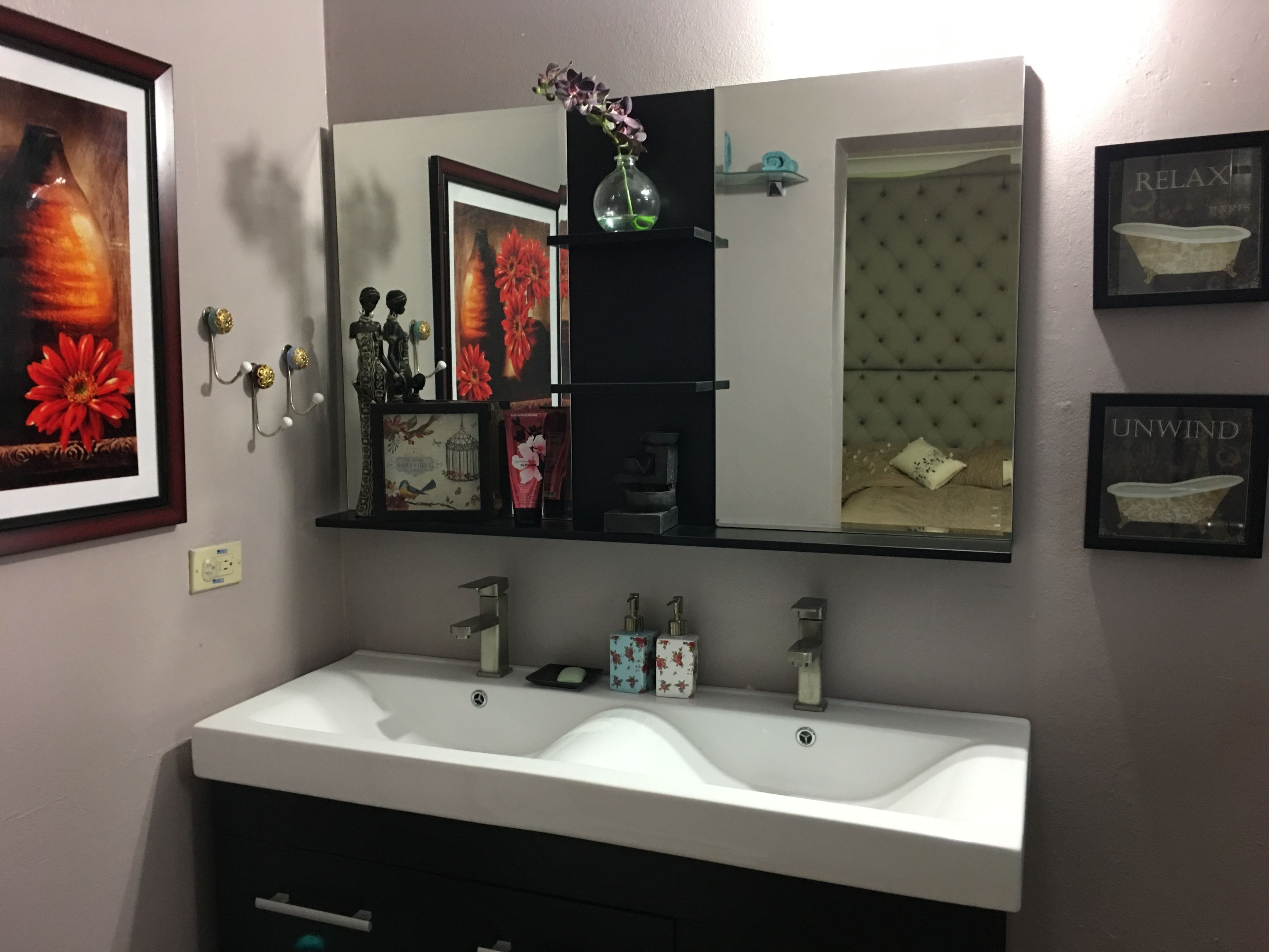 Un bagno con uno specchio grande, un lavandino bianco e diversi oggetti decorativi, tra cui quadri incorniciati e un vaso.