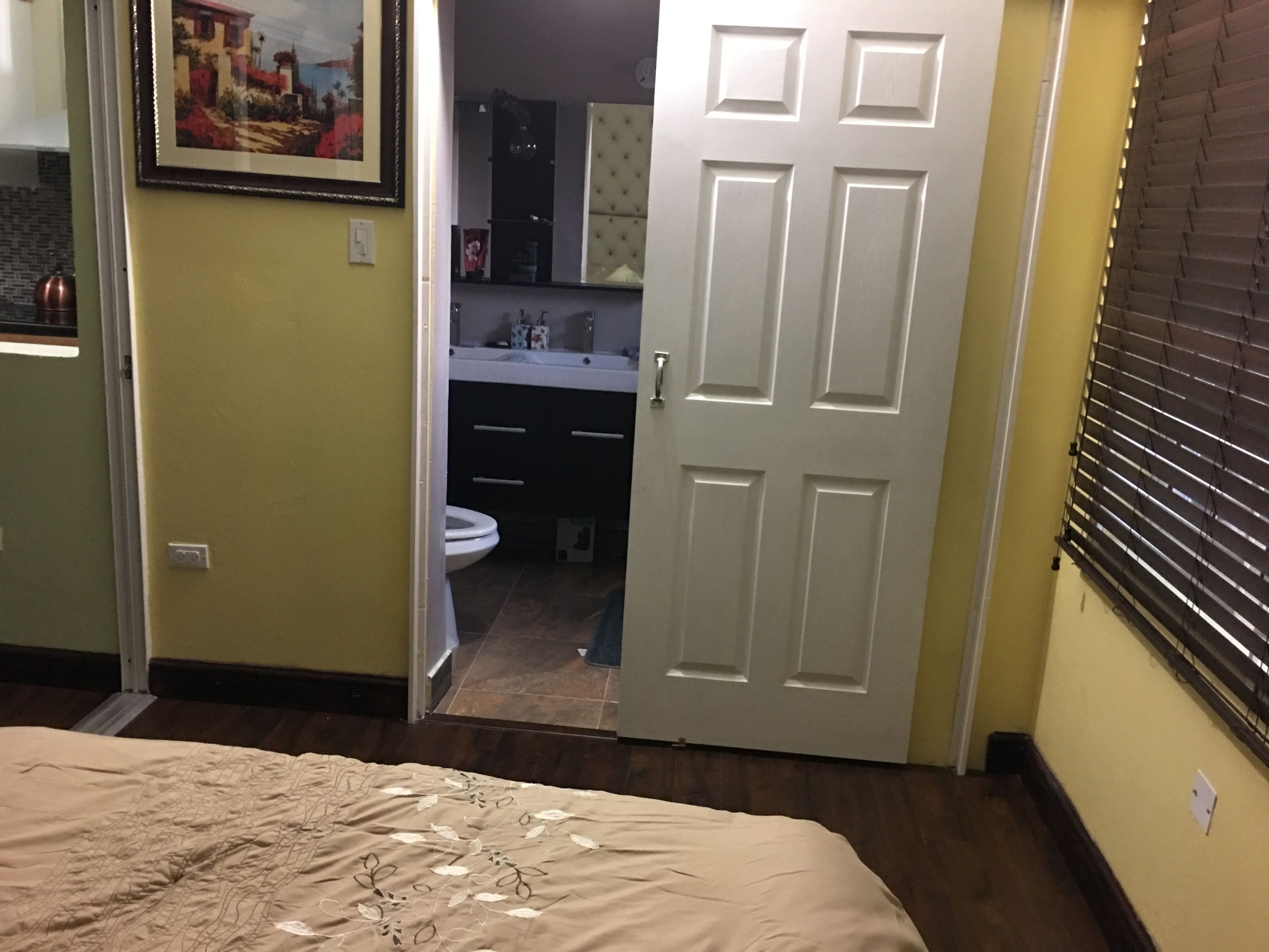 A bedroom with a bed, a door leading to a bathroom, and a window with blinds.