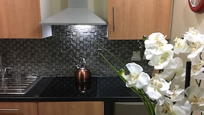 Una cocina con encimera negra, un hervidor de cobre y un jarrón con orquídeas blancas.