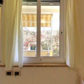 Una habitación con un ventanal, cortinas y vistas a árboles y un edificio.