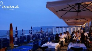 Un restaurante con mesas y sombrillas, con vista a una playa y al océano.