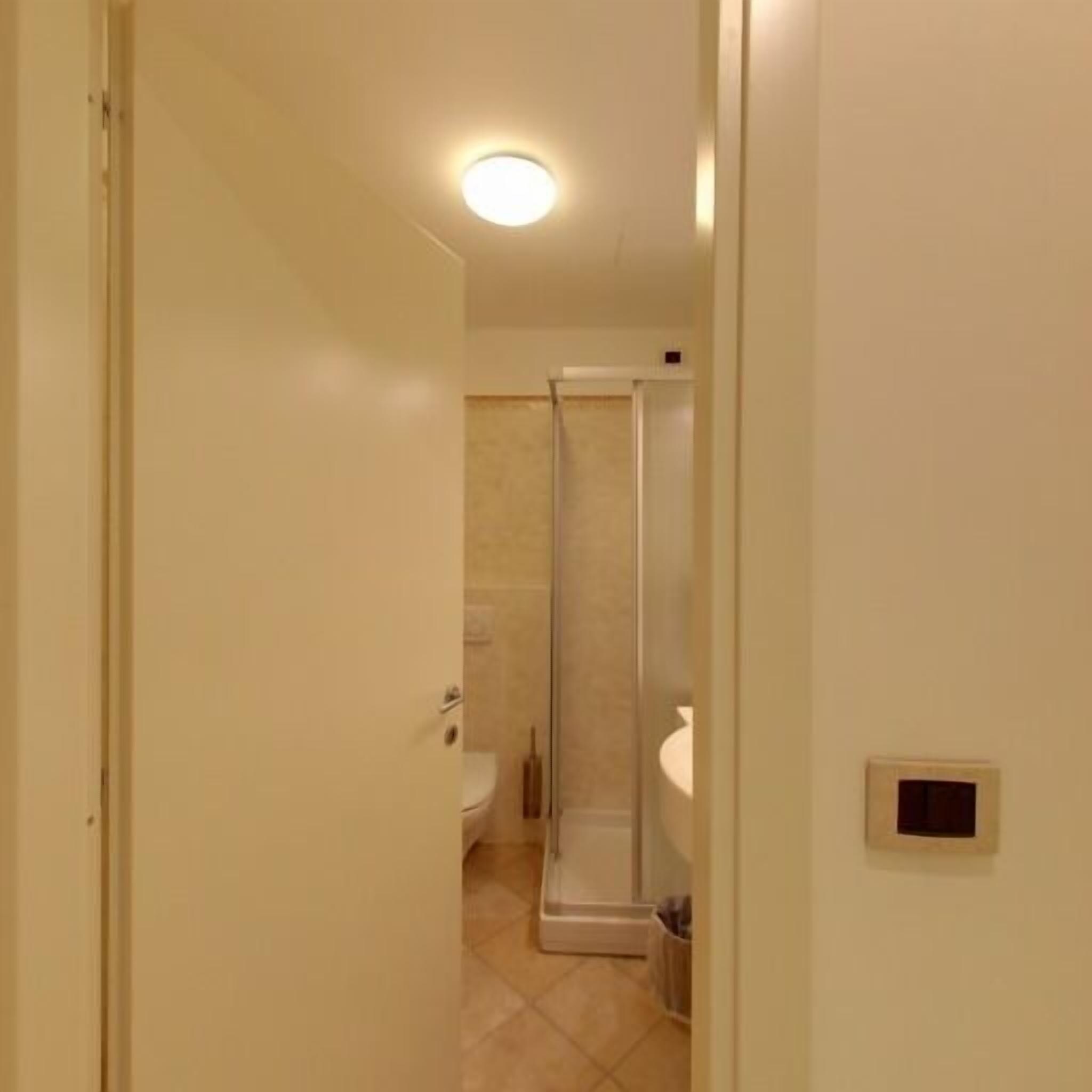 Un corridoio stretto che conduce a un bagno con doccia, wc e lavandino.