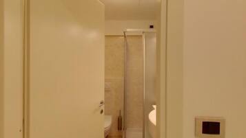 Un corridoio stretto che conduce a un bagno con doccia, wc e lavandino.