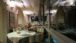 Interior de restaurante con mesas redondas, sillas a rayas y vistas a través de un ventanal.