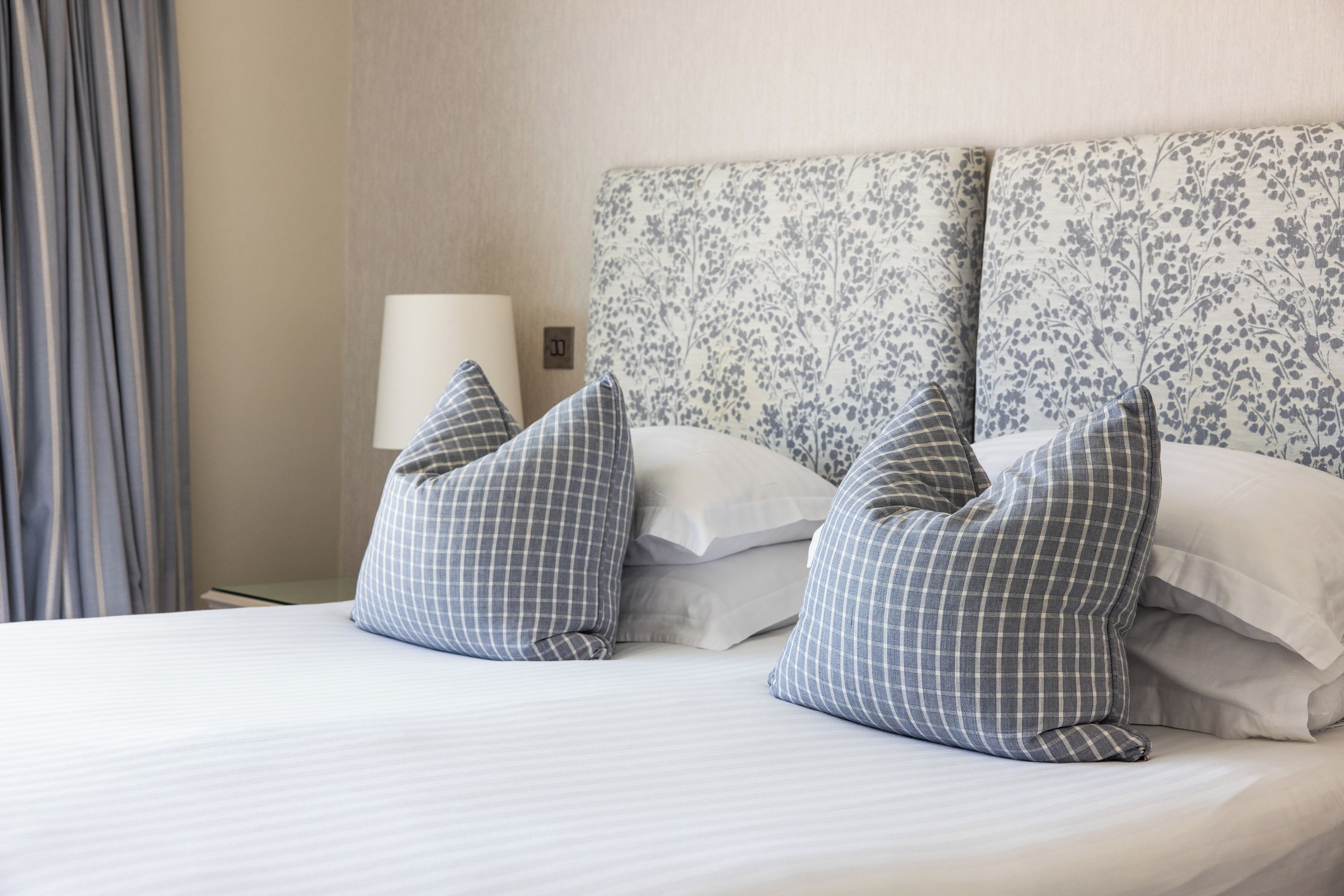 Ein Hotelzimmer mit einem Bett, zwei Kissen, einer Lampe und einem Kopfstück mit Blumenmuster.