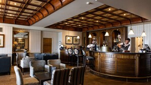 Zona de bar con mostrador de madera, luces colgantes y asientos con sillones tapizados.